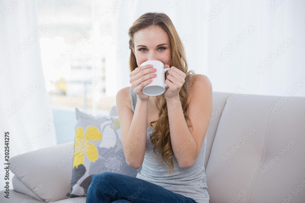 Happy young woman sitting on sofa drinking from a mug Happy young woman sitting on sofa drinking from a mug