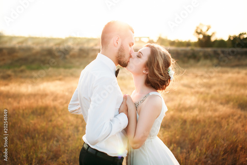Happy wedding couple hugging and kissing. Beautiful young bride and groom, just married. Couple in love. Sunset light, sunshine. Bokeh.