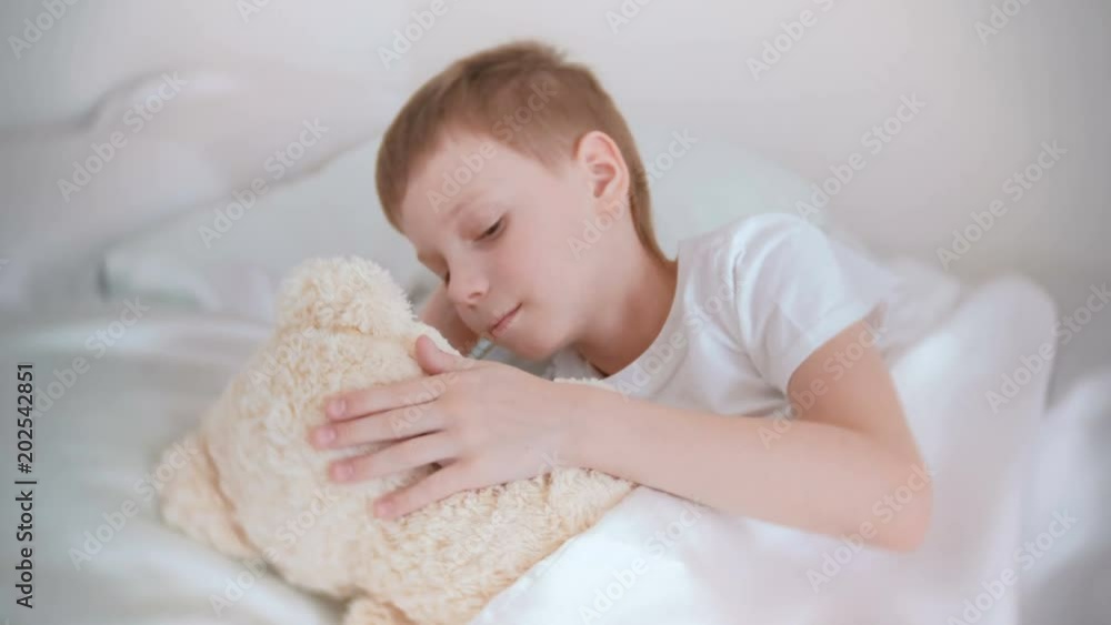 Seven-year-old boy woke up and stroking a toy bear lying in bed. Seven-year-old boy woke up and stroking a toy bear lying in bed.