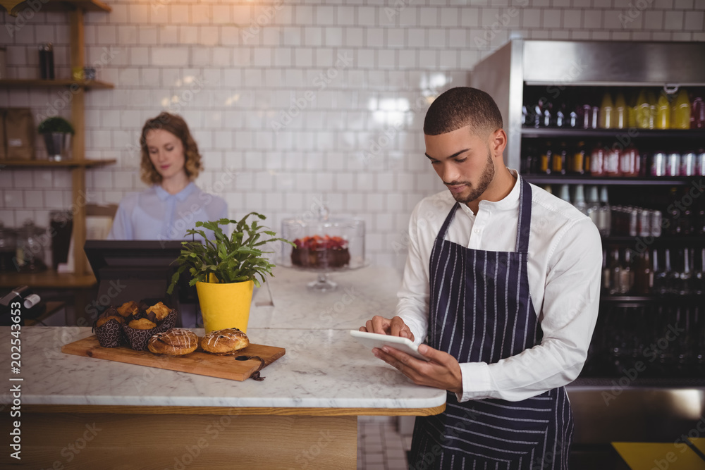 Young waiter using digital tablet while standing by counter