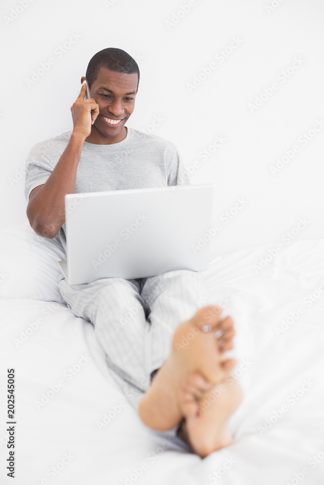 Afro man using cellphone and laptop in bed Afro man using cellphone and laptop in bed