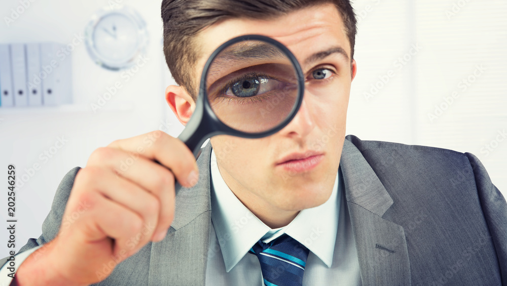 Businessman looking through magnifying glass against a empty office with a laptop Businessman looking through magnifying glass against a empty office with a laptop
