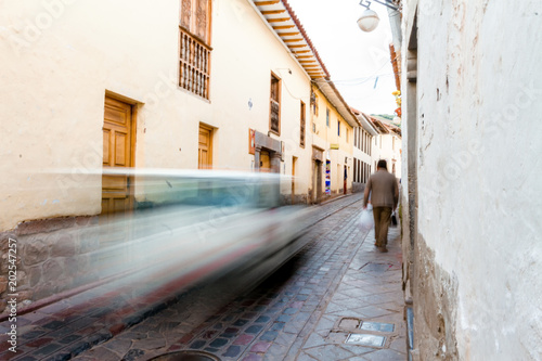 Man walks through the narrow path of an alley in Cusco (Peru) while a car passes quickly © simonmayer