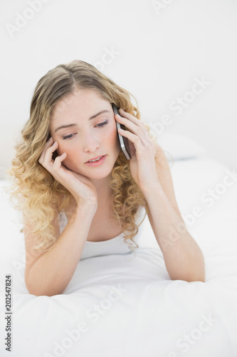 Pretty calm blonde lying on bed phoning