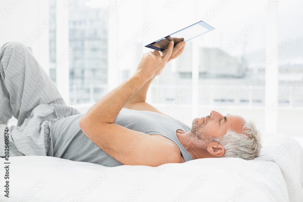 Relaxed mature man using digital tablet in bed Relaxed mature man using digital tablet in bed