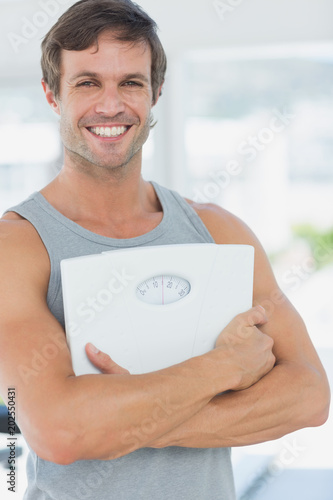 Fit young man with scale in bright exercise room