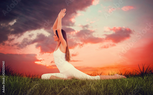 Sporty woman with joined hands over head at a fitness studio against red sky over grass