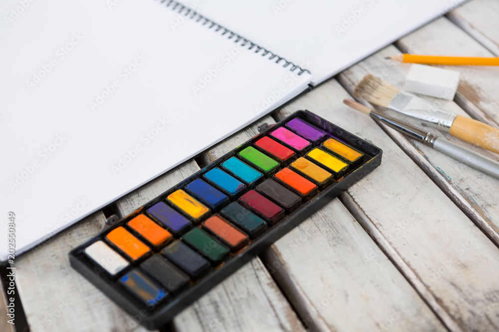Colorful palette, paintbrushes and book on wooden surface Colorful palette, paintbrushes and book on wooden surface