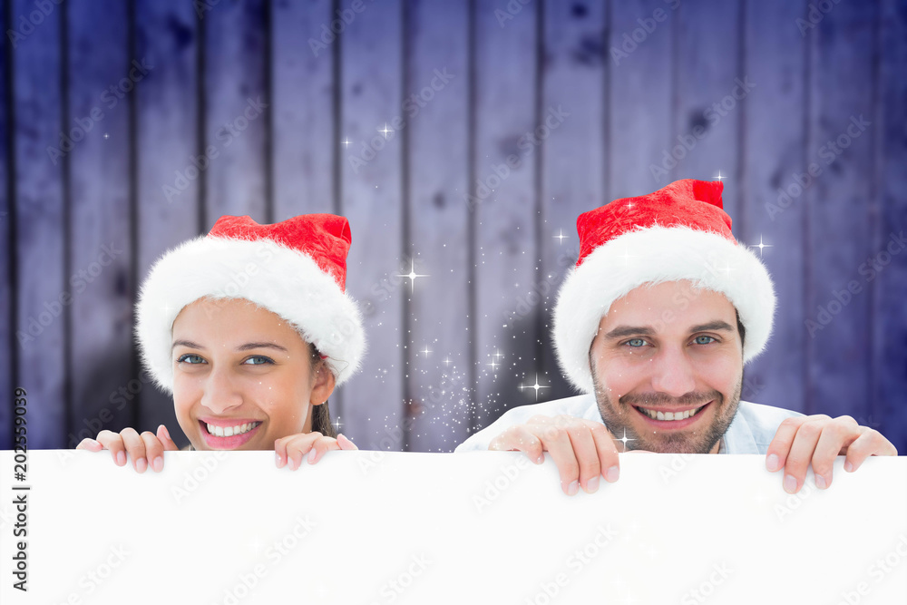 Festive young couple smiling at camera against blurred wooden planks Festive young couple smiling at camera against blurred wooden planks