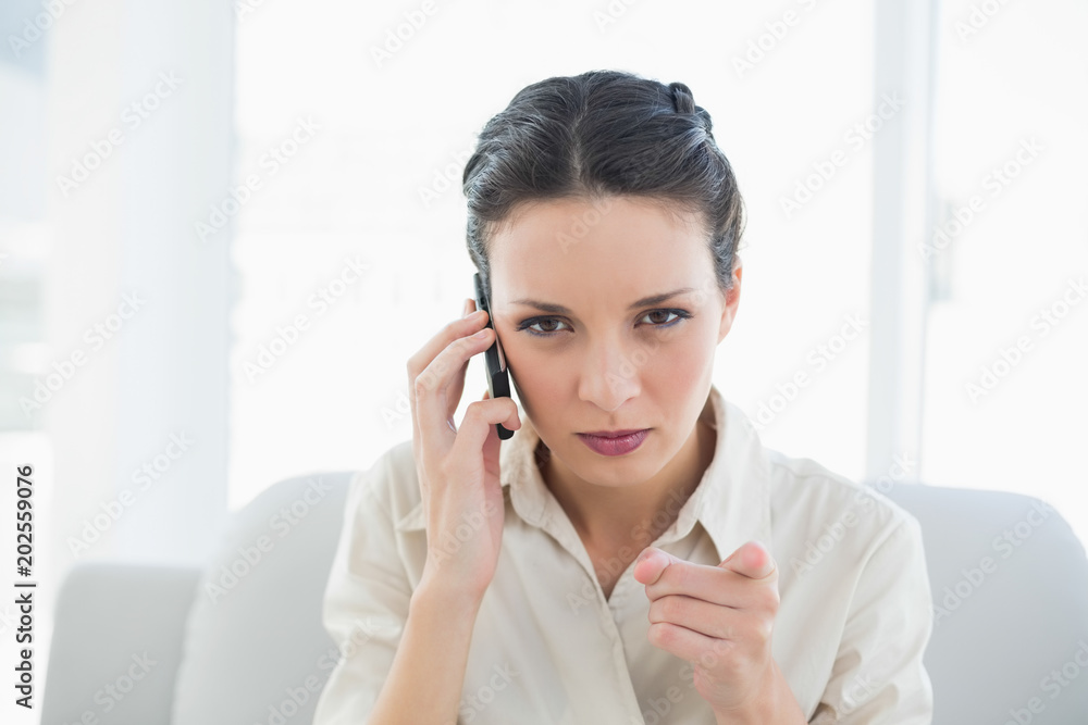 Irritated stylish brunette businesswoman making a phone call and pointing camera with her finger Irritated stylish brunette businesswoman making a phone call and pointing camera with her finger