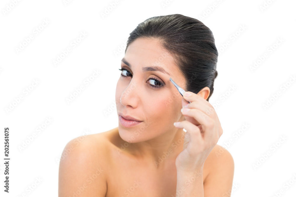 Brunette plucking her eyebrows and looking at camera
