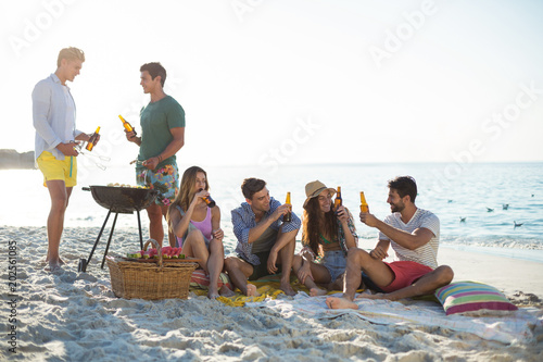 Friends having drinks by barbecue at beach against sky