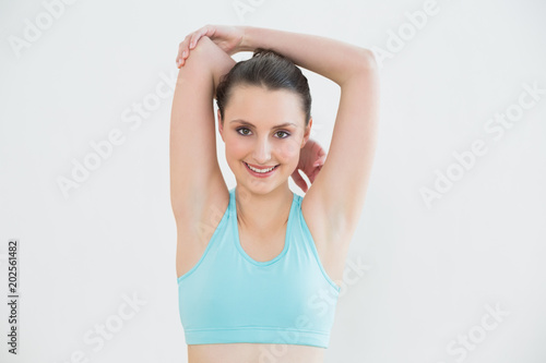 Toned woman stretching hands behind head against wall