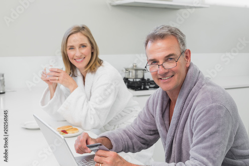Happy couple in bathrobe doing online shopping at home