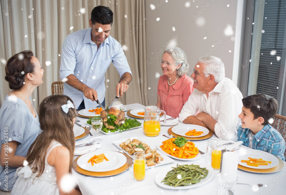Composite image of Extended family at dining table in house against snow falling