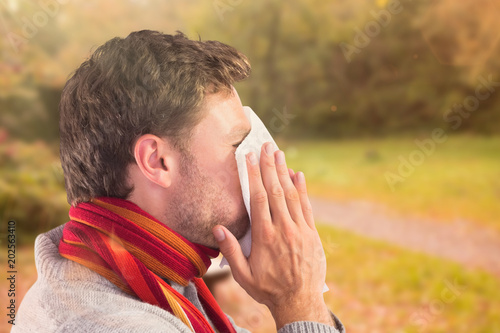 Man blowing nose on tissue against peaceful autumn scene in forest © vectorfusionart