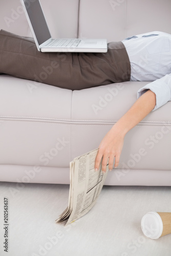 Woman with laptop and news paper lying on sofa