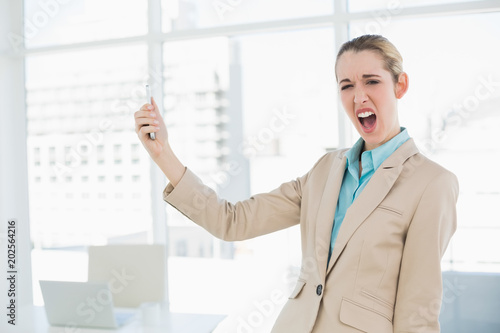 Cute shocked businesswoman holding her smartphone looking at camera