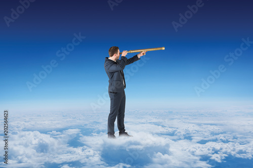 Businessman looking through telescope against blue sky over clouds at high altitude
