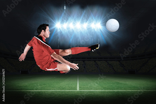 Football player in red kicking in a football pitch under spotlights © vectorfusionart