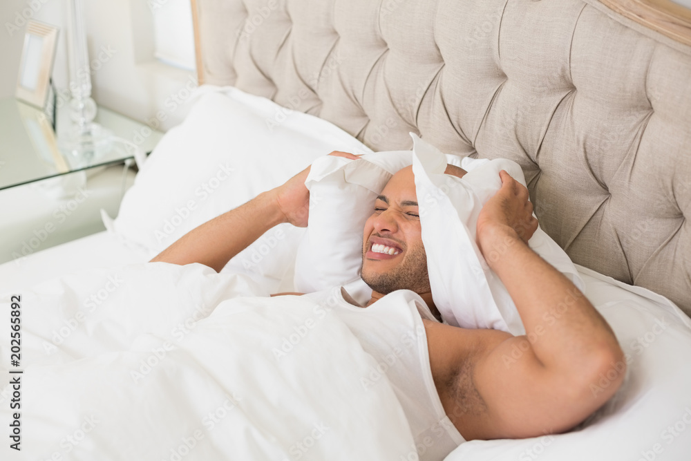 Sleepy man covering ears with pillow in bed Sleepy man covering ears with pillow in bed