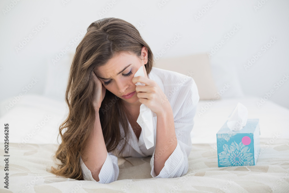 Depressed casual brown haired woman in white pajamas crying on her bed Depressed casual brown haired woman in white pajamas crying on her bed