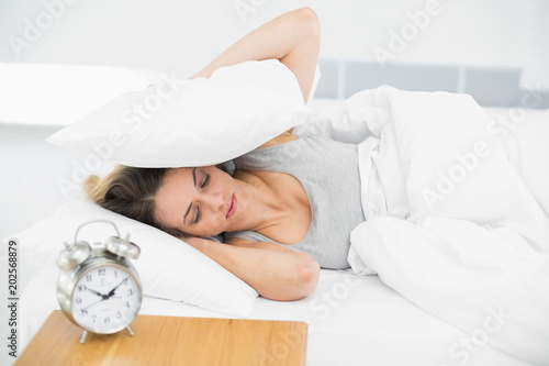 Cute tired woman covering her ears with pillows