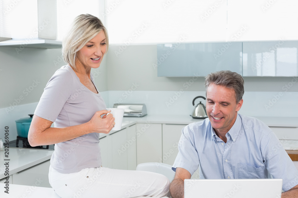 Couple with coffee cup and laptop in kitchen Couple with coffee cup and laptop in kitchen