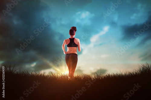 Fit brunette jogging away from camera against blue sky over grass
