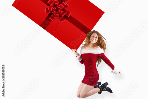 Festive redhead jumping with gift against red christmas ribbon