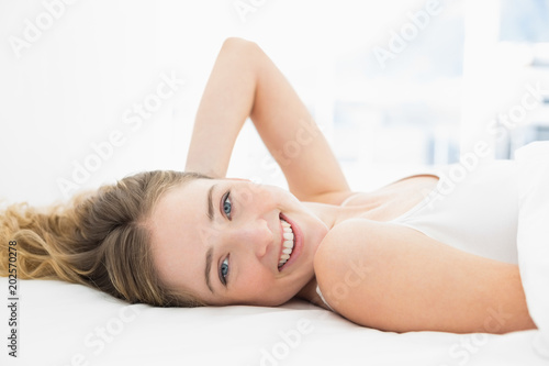 Pretty smiling blonde lying in bed looking at camera