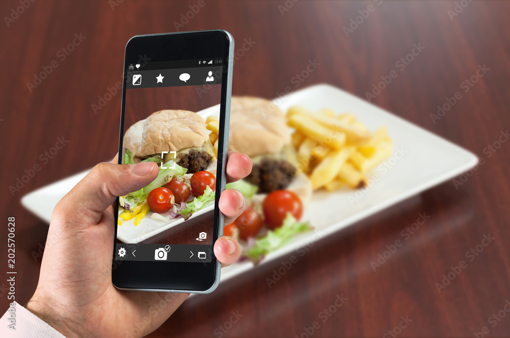 Φωτογραφία hand holding smartphone against side view of burger with french fries and salad