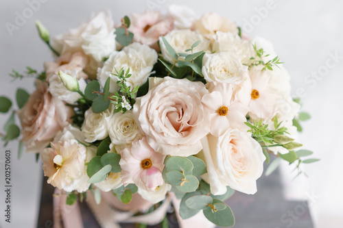 Wedding bouquet of white roses and buttercup on a wooden table. Lots of greenery  modern asymmetrical disheveled bridal bunch