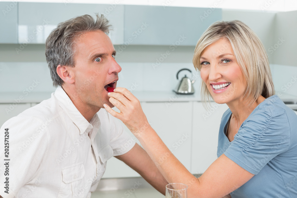 Loving woman feeding man in the kitchen Loving woman feeding man in the kitchen