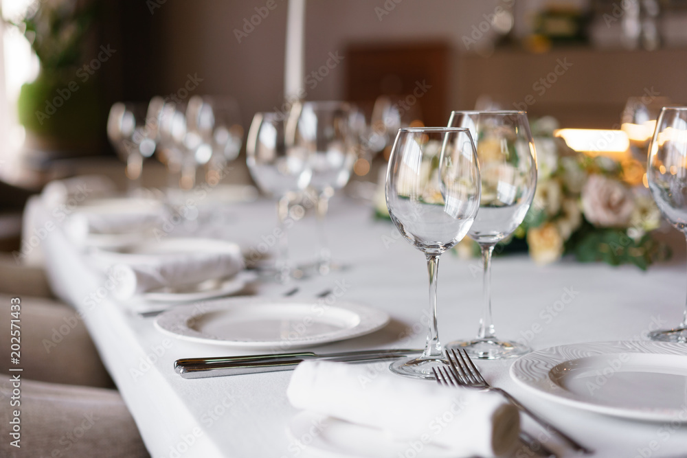 Table setting in the restaurant, glasses in the foreground. Luxury wedding reception. Flower arrangement on table in restaurant. Stylish decor and adorning.