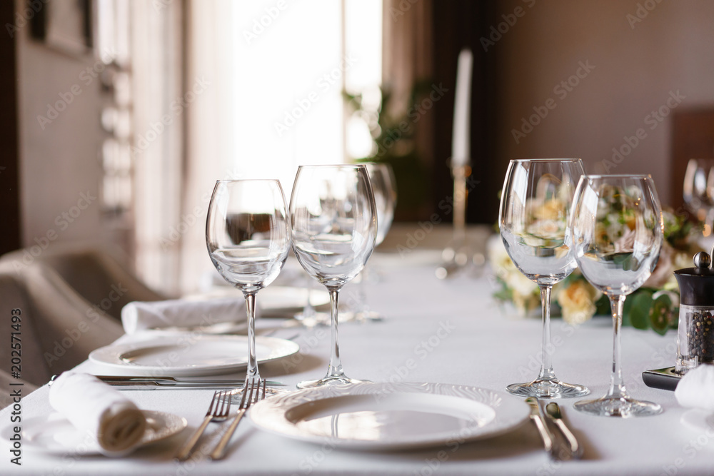 Table setting in the restaurant, glasses in the foreground. Luxury wedding reception. Flower arrangement on table in restaurant. Stylish decor and adorning.