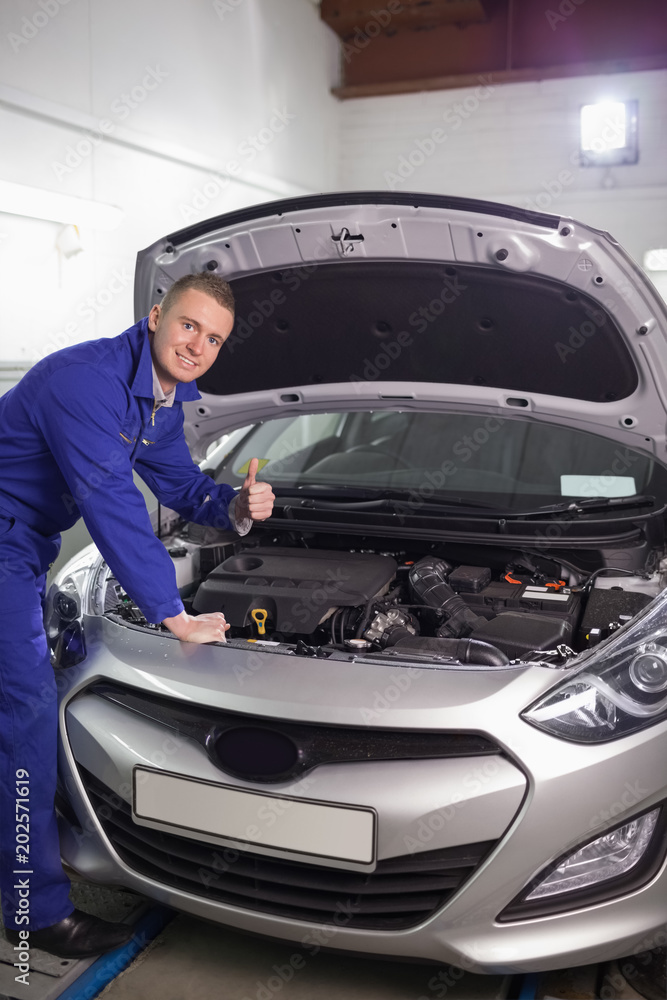 Fototapeta premium Mechanic leaning on a car with his thumb up