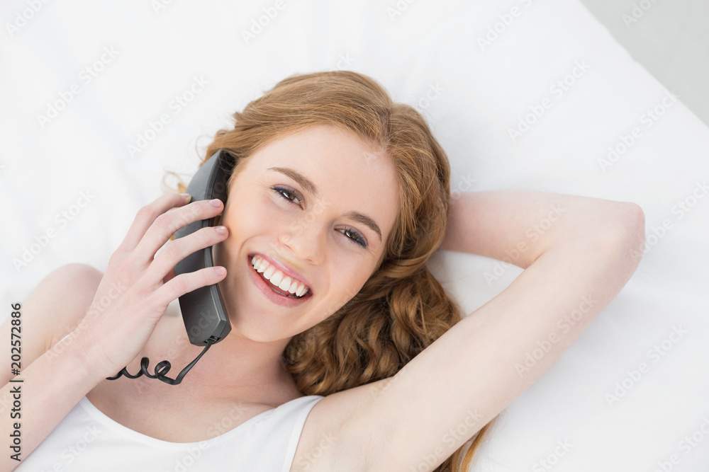 Cheerful young woman using telephone in bed Cheerful young woman using telephone in bed