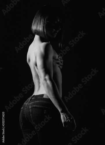 Young female model with muscular body poses on a dark background. black and white