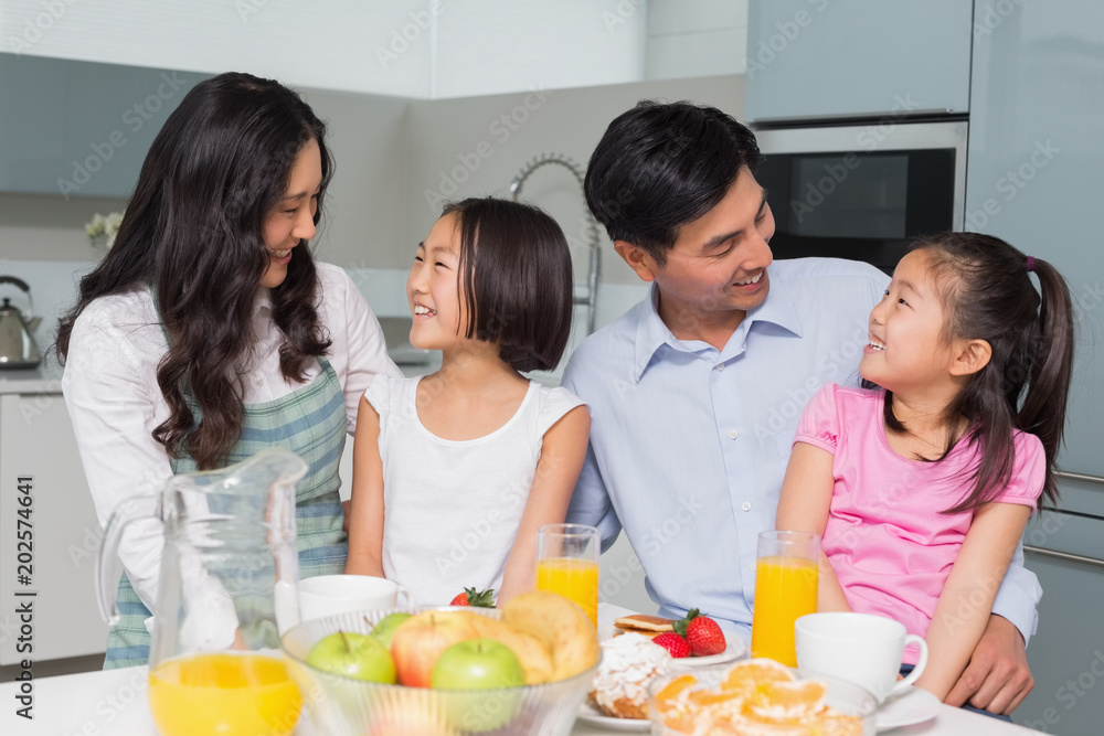 Cheerful family of four enjoying healthy breakfast in kitchen Cheerful family of four enjoying healthy breakfast in kitchen