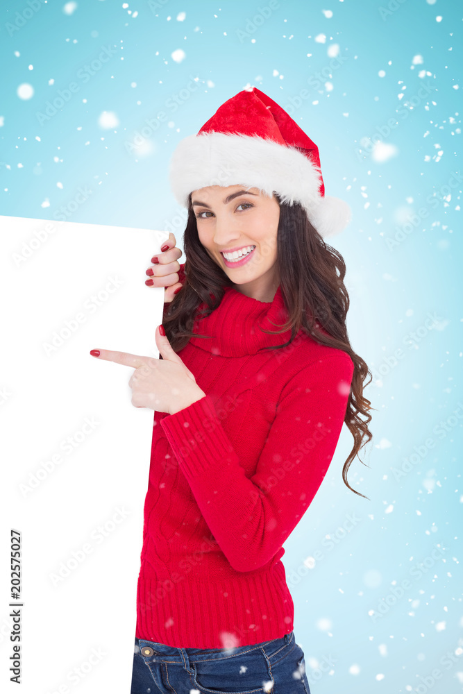 Smiling brunette in santa hat pointing white poster against blue background with vignette Smiling brunette in santa hat pointing white poster against blue background with vignette