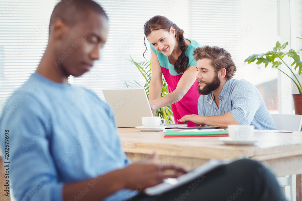 Woman pointing at laptop while discussing with man at desk Woman pointing at laptop while discussing with man at desk