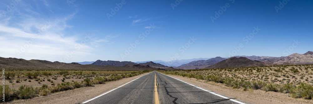panoramic view down a deserted road in death valley national park on a clear blue sky day