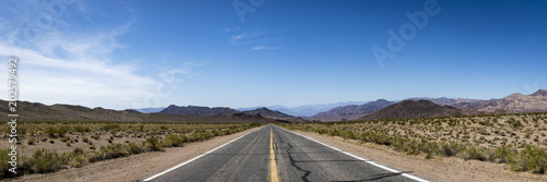 panoramic view down a deserted road in death valley national park on a clear blue sky day
