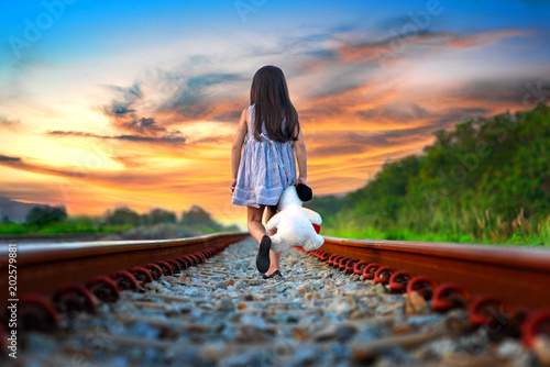 little girl run away from home, walking on railway alone, upset with parent and disappoint mind, sadly walikng with dollmate photo