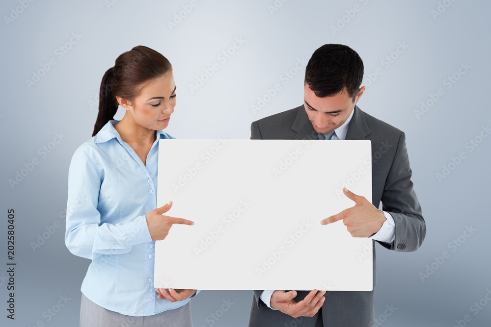 Business partners pointing at sign they are presenting against grey vignette Business partners pointing at sign they are presenting against grey vignette