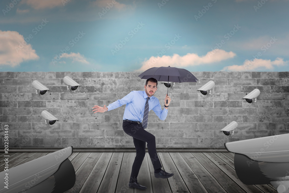 Anxious businessman under umbrella balancing against blue sky over brick wall Anxious businessman under umbrella balancing against blue sky over brick wall