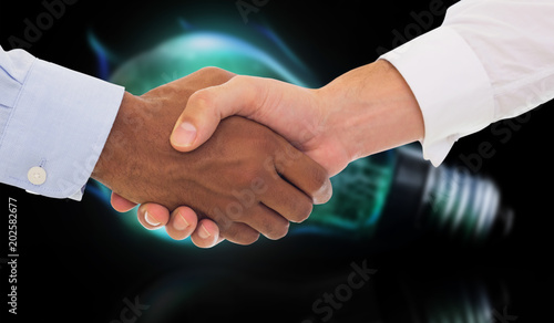 Close-up shot of a handshake in office against glowing light bulb