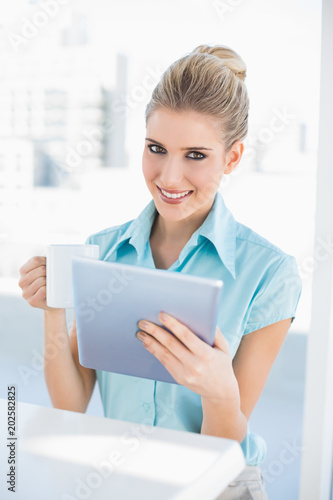 Smiling elegant woman using tablet holding coffee