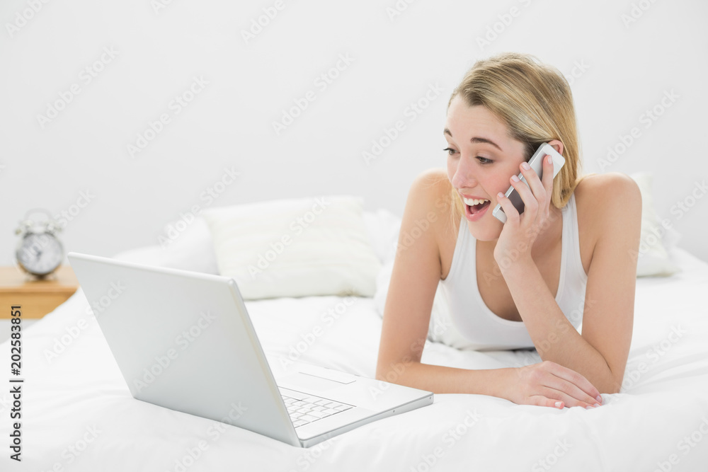 Astonished lovely woman phoning with her smartphone looking at her laptop Astonished lovely woman phoning with her smartphone looking at her laptop